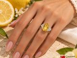 yellow sapphire and diamond ring on a woman ' s hand with lemons in the background
