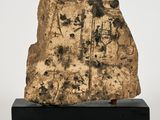 an ancient rock with writing on it sitting on a black stand