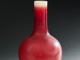 un vase rouge posé sur une table, sur fond noir
