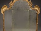 an ornately carved mirror with a gold frame on a grey background