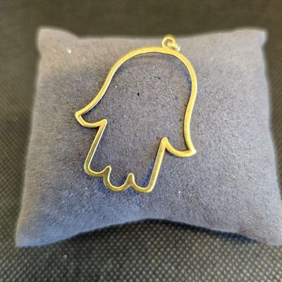 un petit pendentif en forme de main de Hamsa en or posé sur un oreiller