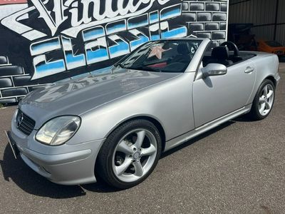 une Mercedes SLK cabriolet argentée garée devant une pancarte « Vintage Fix »