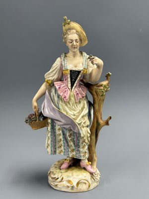une figurine ancienne représentant une femme assise sur une branche d'arbre, tenant un panier