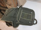 a green backpack sitting on the floor next to a pile of clothes