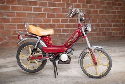 a small red motorcycle parked in front of a brick wall