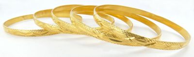 trois bracelets en or posés sur une surface blanche, sur fond blanc
