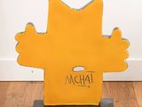 mustard colored cat sculpture on wooden stand with white wall and wood flooring