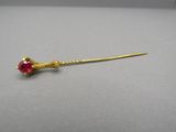 a close up of a gold stick with a red stone on it