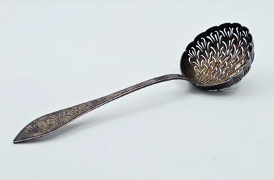 une cuillère en argent avec un manche en métal posée sur une surface blanche