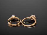 two gold rings with diamonds and pearls on a black surface