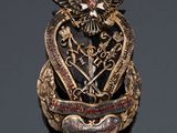 an image of a gold and red broochle with a bird on it