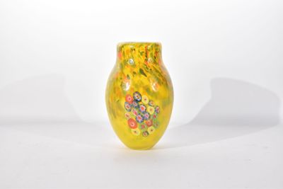 un vase jaune orné de fleurs, posé sur une surface blanche