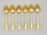 six gold spoons and a spoon rest on a white surface