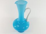 a blue glass vase with a white handle on a white surface