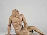 statue of a naked man sitting on a wooden base