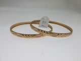 two gold bang bracelets with engraved designs on them
