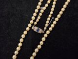 un collier de perles blanches muni d'un fermoir en argent, sur fond noir