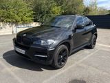 La BMW X6 est garée sur un parking, avec des arbres en arrière-plan.