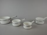 four white bowls and spoons are lined up on a gray surface