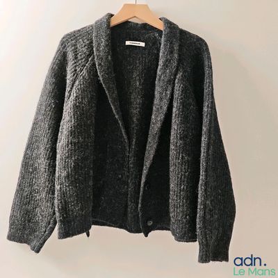 un cardigan gris suspendu à un cintre devant un mur blanc