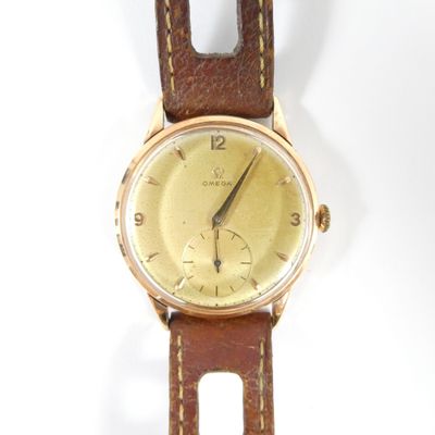 une montre en or avec un bracelet en cuir marron sur un fond blanc