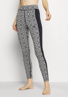 Une femme vêtue d'un legging à motifs noirs et blancs se tient debout devant un mur blanc.