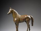 statue of a horse standing on a wooden base against a gray background