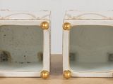 pair of white and gold ceramic boxes with gold accents on top of a table