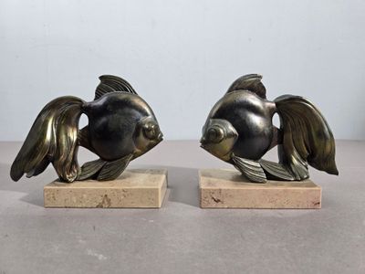 une paire de sculptures de poissons en bronze posées sur des socles en marbre, disposées sur une table