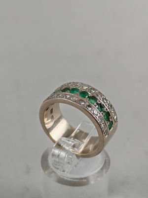 a close up of a diamond and emerald ring on a clear surface