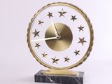 horloge dorée et blanche ornée d'étoiles, posée sur un socle en marbre, sur fond blanc