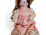 une vieille poupée assise par terre, vêtue d'une robe rose et d'un chapeau de paille