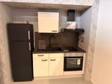 une petite cuisine avec un réfrigérateur noir et des placards blancs