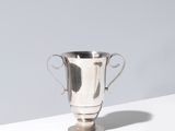 une coupe de trophée plaquée argent posée sur une table blanche devant un mur gris