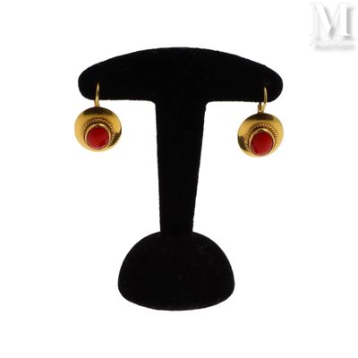 une paire de boucles d'oreilles rouges et dorées posées sur un présentoir noir