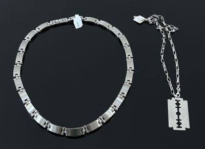 un collier composé de deux pièces d'argent et une lame de rasoir posés sur une surface noire
