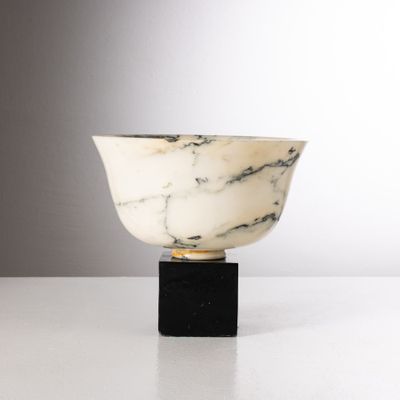un bol en marbre blanc avec un socle noir posé sur une surface blanche
