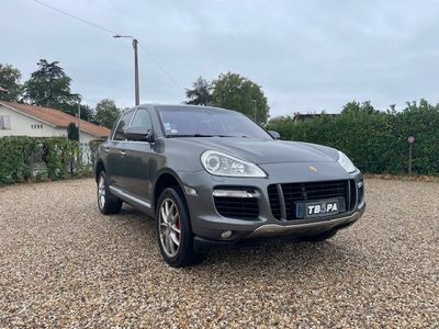 a grey porsche cayen is parked in a gravel parking lot