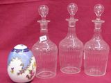 three clear glass bottles and a small vase sitting on a red cloth