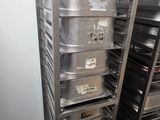 several trays of food are stacked on a metal rack in a kitchen