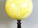 un globe jaune posé sur un socle noir, lui-même posé sur une surface blanche