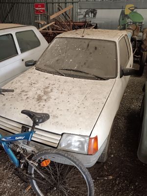 a dirty white car and a blue bicycle in a junkyard