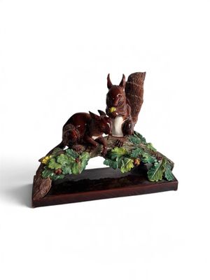 figurine représentant un écureuil perché sur une branche, une noisette dans la bouche