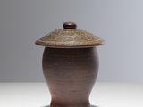 une photo d'un vase marron muni d'un couvercle, posé sur une table