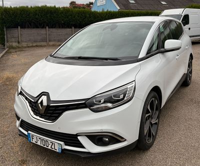 La voiture blanche est garée sur le parking, à côté d'une camionnette.