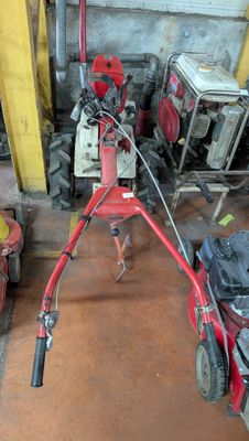 une tondeuse à gazon rouge dans un garage, à côté d'autres outils