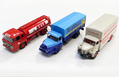 trois camions miniatures posés les uns à côté des autres sur une surface blanche
