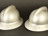 two silver hard hats sitting on top of each other on a black surface