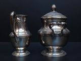 two silver vases sitting on a table with a black background