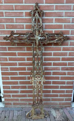 une croix en métal posée par terre près d'un mur de briques